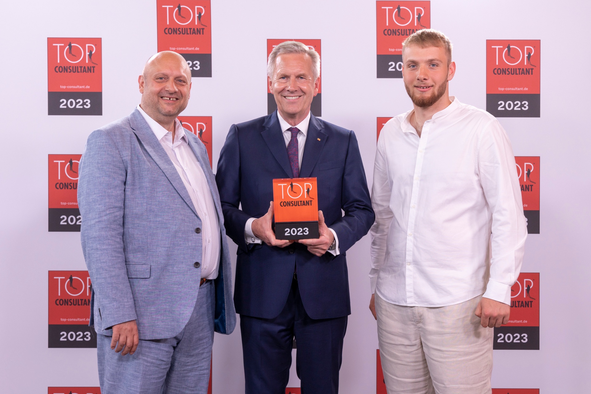 Preisverleihung Top Consultant 2023: Peter Saubert, Bundespräsident a.D. Christian Wulff und Willi Saubert vor der Top-Consultant-Fotowand